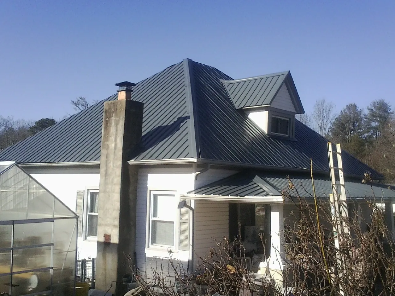 Dark blue standing seam metal roof on a white farmhouse with dormer — Slate & Tile Roof Repair by Roofing Brothers in Gates Mills