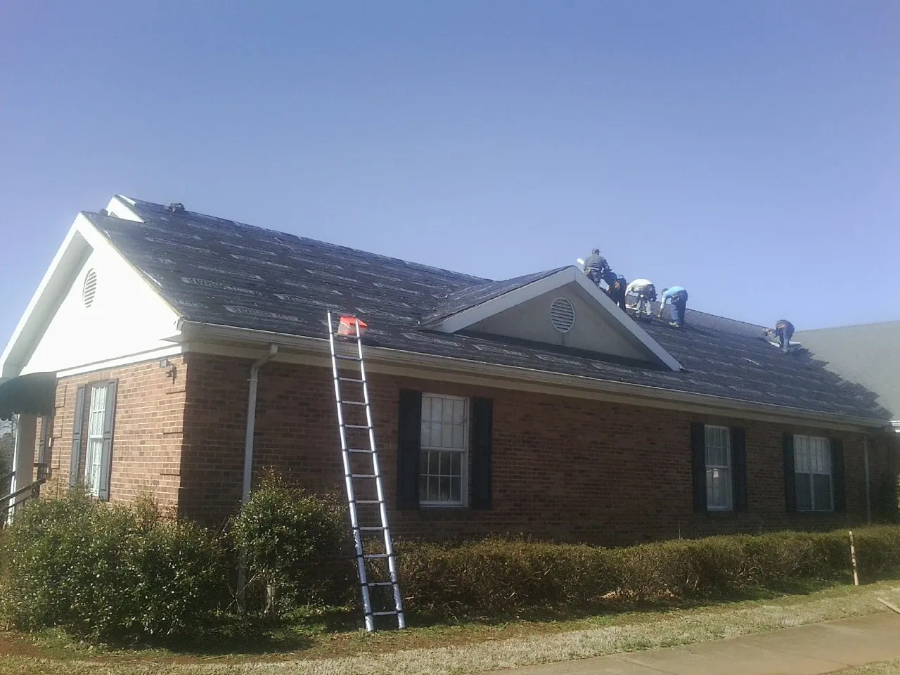 Crew tearing shingles off a brick ranch roof with a ladder set — Emergency Roof Repair work by our crew in Gates Mills