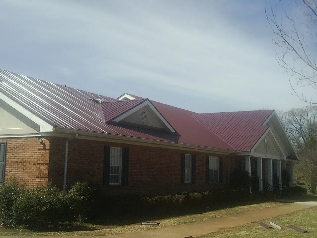 Red metal roof with gabled entries on a long brick building, from a Hail Damage Roof Repair job in Gates Mills