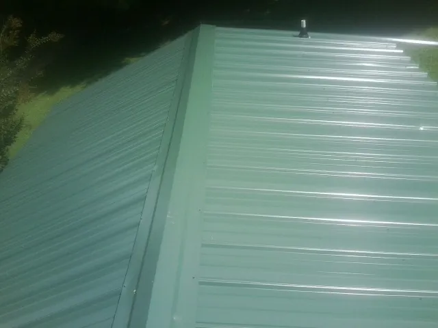 New green metal panels meeting at the ridge of a roof — Flat Roof Repair work by our crew in Gates Mills