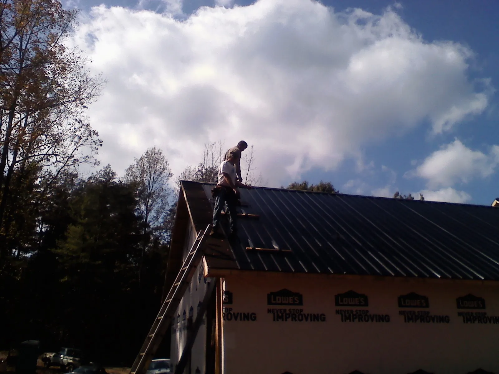 Roofer fastening dark metal panels high against a cloudy sky, from a Roof Inspection job in Gates Mills