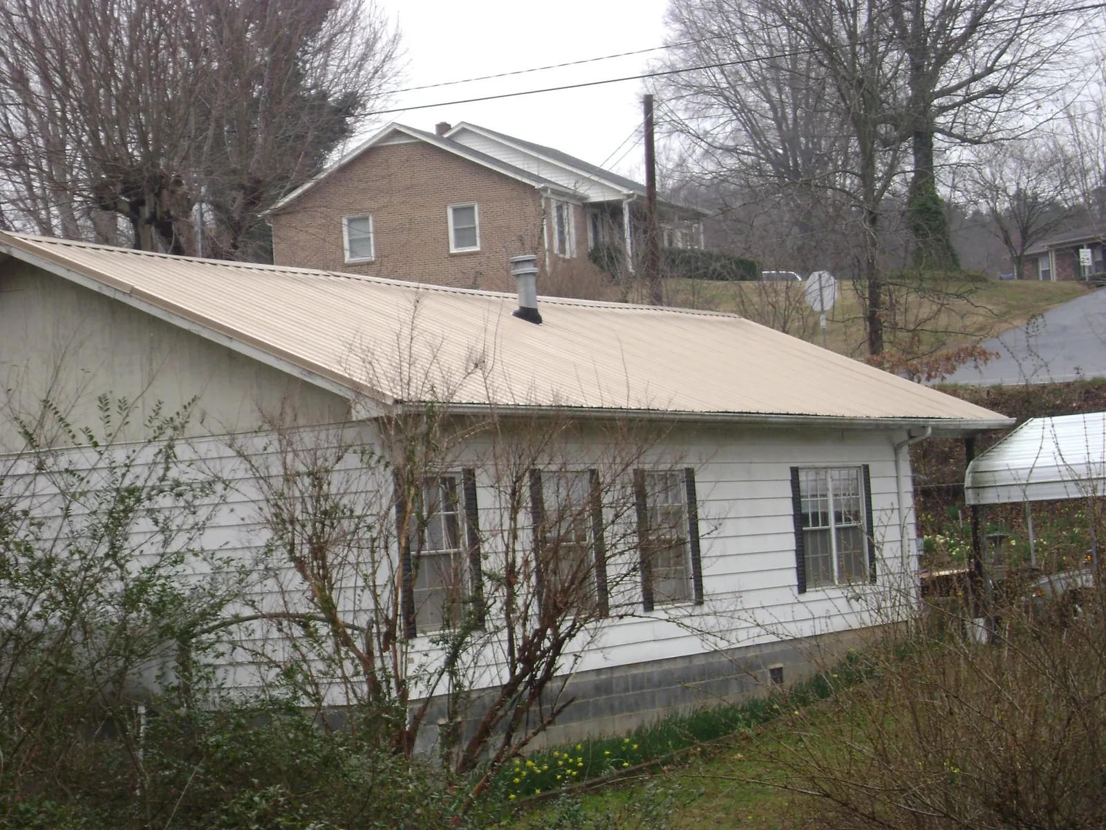 Tan metal roof on a white sided house set into a hillside — Commercial Roofing by Roofing Brothers in Gates Mills