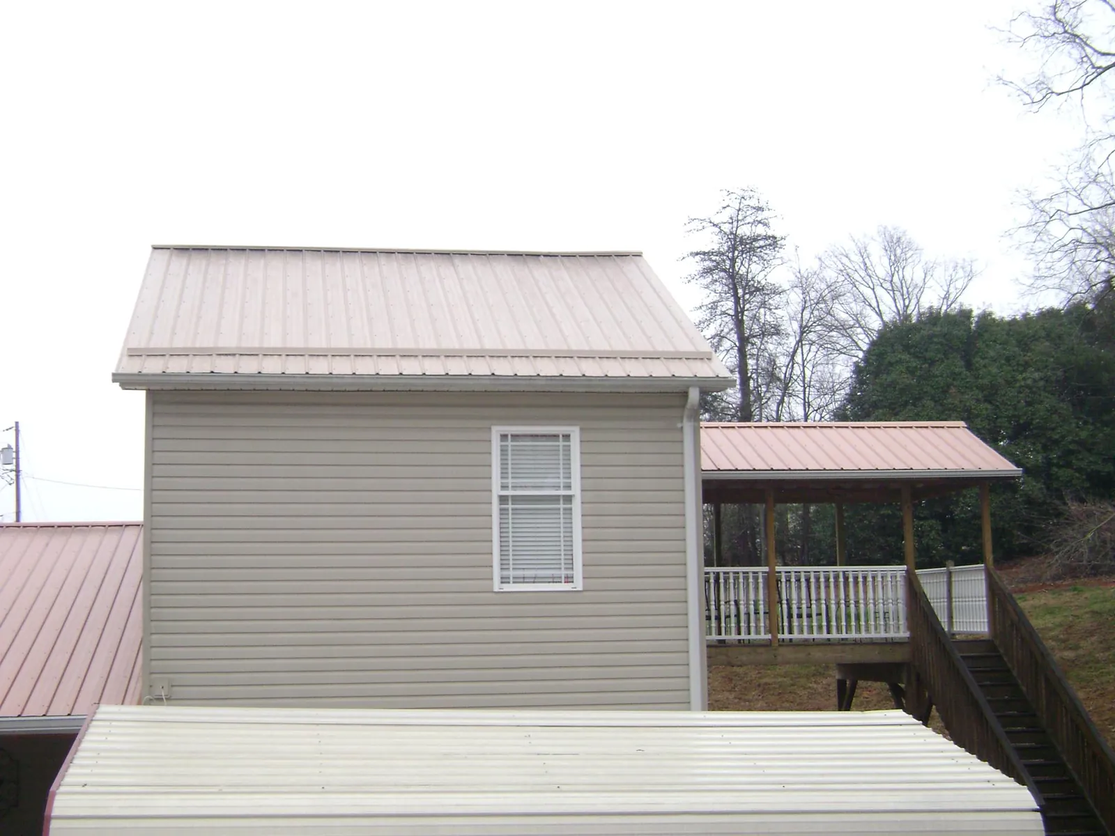 Tan metal roofs on a two story addition and attached porch, from a Roof Replacement job in Gates Mills